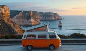 Un camping-car orange avec toit relevable sur une falaise portugaise. Idéal pour un budget pour aller au Portugal en camping-car.