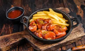 Currywurst et frites, un classique pour savoir où manger à Berlin. Servi dans une poêle en fonte avec une sauce tomate épicée et du curry en poudre.