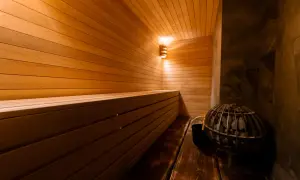 Intérieur d'une **sauna Prague** chaleureuse, avec des bancs en bois clair, un poêle à pierres et un éclairage doux.
