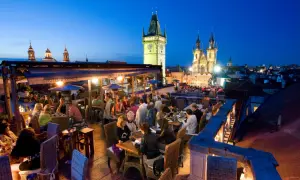 Dîner sur un rooftop à Prague, avec vue sur la tour de l'horloge et l'église Notre-Dame du Týn. Ambiance chaleureuse.