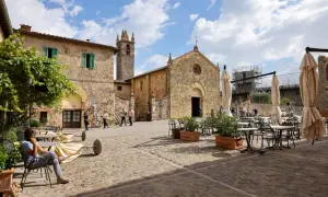 Place pavée de Monteriggioni, Italie, avec une église médiévale et des tables de café.