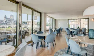 Salle lumineuse avec vue panoramique sur la Loire. Tables dressées, chaises bleues confortables. Un cadre idéal pour découvrir les restaurants de la Loire.