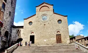 Le majestueux **duomo San Gimignano** se dresse sous un ciel bleu éclatant, ses marches invitant à la découverte de son histoire.