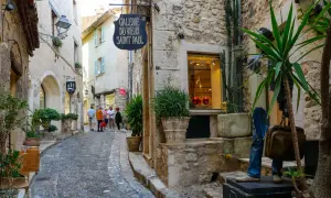 Ruelle pavée à Saint-Paul-de-Vence, avec des boutiques, des plantes et des touristes.
