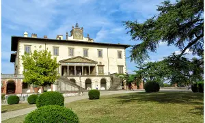 La villa Poggio a Caiano, un joyau architectural, se dresse sous un ciel bleu. Des arbres majestueux ombragent la pelouse verdoyante et les buissons taillés.
