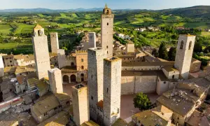 Vue aérienne de San Gimignano, avec ses tours médiévales emblématiques se dressant au-dessus des toits de tuiles, le tout baigné par la lumière dorée du soleil toscan.