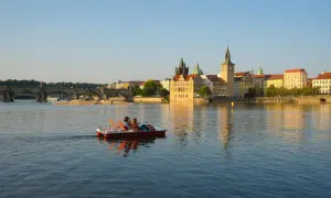 Un couple profite d'une balade en pédalo sur la Vltava, offrant une perspective insolite de Prague et de son pont emblématique au coucher du soleil.