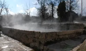 Bains antiques en pierre à San Casciano dei Bagni, dégageant une vapeur d'eau chaude sous un ciel bleu.