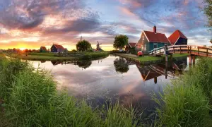 Coucher de soleil sur un canal bordé de roseaux, avec des moulins et des maisons traditionnelles, un aperçu des plus belles villes des Pays-Bas.