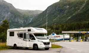 Camping-car blanc prêt pour un road trip en Norvège en camping-car budget, avec un ferry et des montagnes en arrière-plan.