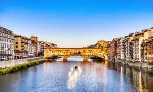 Le Ponte Vecchio, avec ses boutiques colorées, enjambe l'Arno sous un ciel bleu. Une petite barque glisse sur l'eau.