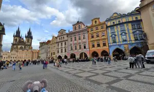 Une souris en peluche explore la place de la Vieille Ville de Prague, avec la tour de l'église Notre-Dame devant le Týn en arrière-plan.
