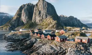 Village de pêcheurs aux maisons rouges sur pilotis, dominant la mer, avec une montagne imposante en arrière-plan. Idéal pour un circuit Lofoten 6 jours.