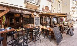 Terrasse d'un restaurant "Bar à Vin" dans le restaurant bonifacio vieille ville. Tables dressées, chaises noires, ardoises de menu. Ambiance estivale.