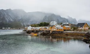 Maisonnettes jaunes sur pilotis, reflets dans l'eau, montagnes brumeuses en arrière-plan. Idéal pour un budget voyage îles Lofoten.
