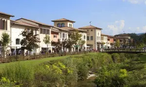Boutiques colorées le long d'une rivière à Barberino di Mugello, avec des passants sur un pont en bois.