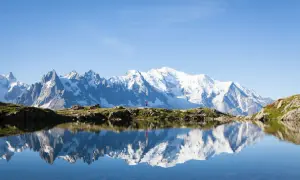 Un randonneur en rouge célèbre la beauté de cet endroit paradisiaque en France, avec le Mont Blanc majestueux se reflétant dans un lac alpin paisible.