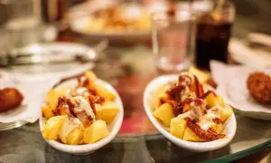 Patatas bravas, un classique pour savoir où manger à Barcelone. Des tapas savoureuses sur une table en verre.