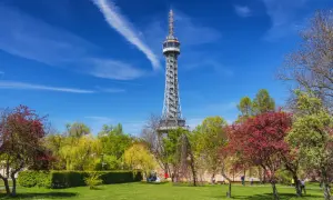 La tour Eiffel de Prague, une structure métallique imposante, se dresse fièrement au milieu d'un parc verdoyant et fleuri sous un ciel bleu éclatant.