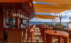 Bar de plage à Cannes avec vue sur la mer. Tables en bois, tabourets de bar et voiles d'ombrage.
