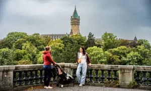 Deux femmes discutent près d'une poussette, avec une vue sur le Palais de la Banque d'État. Un aperçu de ce que l'on peut voir en visiter le Luxembourg en 3 jours.