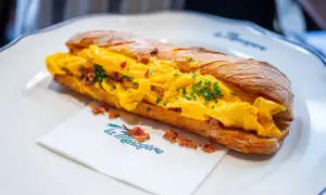 Sandwich aux œufs brouillés et bacon, parfait pour savoir où manger à Florence. Servi sur une assiette blanche avec une serviette "La Ménagère".