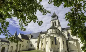 Le majestueux **château de Fontevraud**, avec sa tour imposante et ses arcs romans, se dresse sous un ciel bleu parsemé de nuages, encadré par le feuillage verdoyant des arbres.