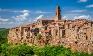 Vue panoramique de Magliano in Toscana, un village médiéval perché sur une falaise, avec ses maisons en pierre et son clocher imposant sous un ciel bleu.