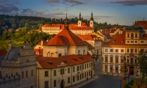 Vue panoramique de Prague au coucher du soleil, avec les toits rouges et les tours du monastère de Strahov dominant le paysage.