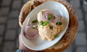 Un plat de fromage à tartiner avec des oignons rouges et de la ciboule, servi avec un bretzel salé, parfait pour un beer garden.