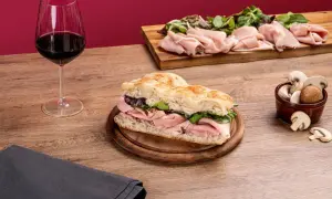 Une délicieuse schiacciata garnie de jambon et de verdure, accompagnée d'un verre de vin rouge et de champignons frais.