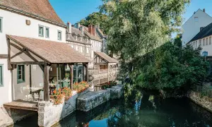Maison ancienne au bord d'une rivière, idéale pour visiter Chartres à pied. Fleurs rouges et reflets dans l'eau.