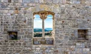 Fenêtre médiévale à Campiglia Marittima offrant une vue sur la mer et les toits du village.