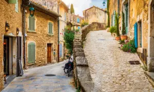 Ruelle pavée d'un village du Luberon, maisons en pierre ocre, volets verts et bleus, fleurs colorées. Parfait pour un week-end Luberon.