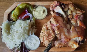 Un plat tcheque copieux : un jarret de porc rôti à la peau croustillante, servi avec de la choucroute, des poivrons, des oignons rouges et deux sauces.