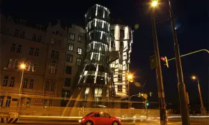 La **maison dansante Prague** s'illumine la nuit, une voiture rouge passe devant, créant une scène urbaine animée.