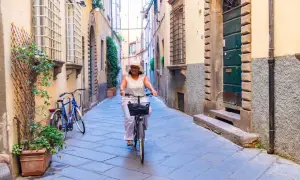Une femme souriante fait du vélo dans une ruelle pavée, profitant d'une belle journée à Florence.