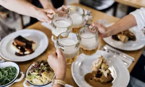 Des mains portent des chopes de bière pour trinquer, autour d'une table garnie de plats traditionnels. Un vrai petit déjeuner à Prague.