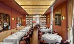 Intérieur d'un restaurant typique Milan, tables dressées, murs corail, étagères à vin illuminées et plafond dorée.