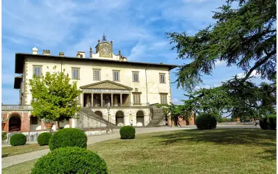 La villa Poggio a Caiano, un joyau architectural, se dresse sous un ciel bleu. Des arbres majestueux ombragent la pelouse verdoyante et les buissons taillés.
