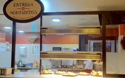 Un comptoir de restaurant à Madrid, avec un panneau "Entrega de Montaditos". Des plats appétissants sont exposés, parfaits pour savoir où manger à Madrid.