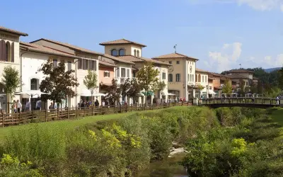 Boutiques colorées le long d'une rivière à Barberino di Mugello, avec des passants sur un pont en bois.