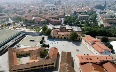 Vue aérienne d'une ville avec des bâtiments historiques et une nouvelle structure moderne, la Fortezza da Basso, ornée de verdure.