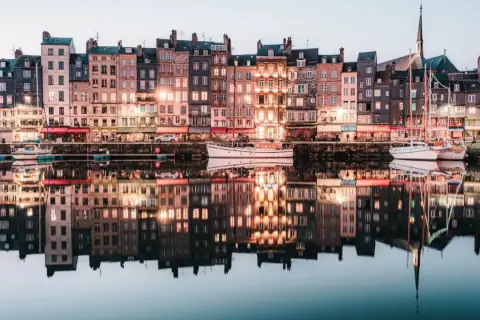 Les maisons colorées de Honfleur se reflètent dans l'eau calme, parfait pour un weekend. Bateaux amarrés, lumières douces.
