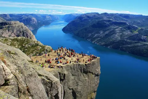 Vue spectaculaire sur un fjord norvégien, avec des randonneurs profitant du paysage. Un souvenir parfait de notre road trip Scandinavie 2 semaines.