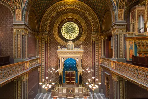 Intérieur orné de la synagogue espagnole de Prague, avec un vitrail circulaire, un Aron Kodesh bleu et des lustres dorés.