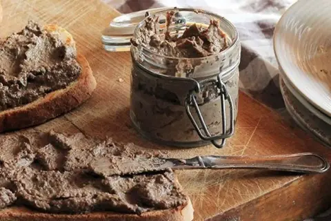 Des toasts tartinés de pâté, prêts à déguster. Un pot de crostini toscani et une assiette de crostini empilés complètent cette scène gourmande.