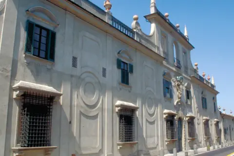 Façade d'une villa à Sesto Fiorentino, avec des fenêtres à volets verts et des ornements circulaires sur le mur.