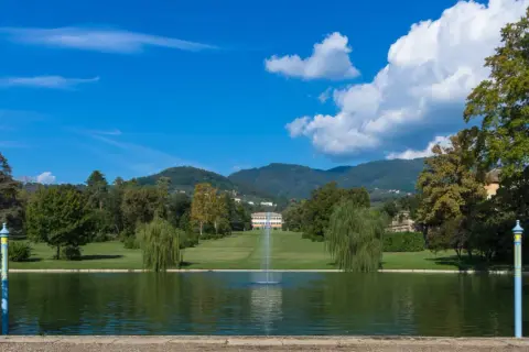Le parc de la villa reale di Marlia s'étend devant un étang paisible, avec une fontaine jaillissant au centre. Des arbres majestueux bordent la pelouse menant à la villa.