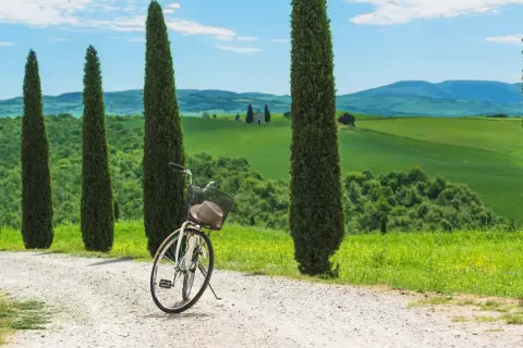 Vélo prêt pour une exploration de la Toscane à vélo, avec des cyprès élancés et des collines verdoyantes en arrière-plan.